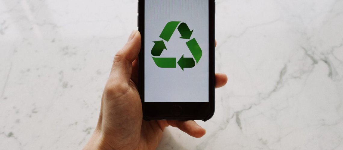 From above view of faceless person holding mobile phone with white screen and green recycle logo above marble surface